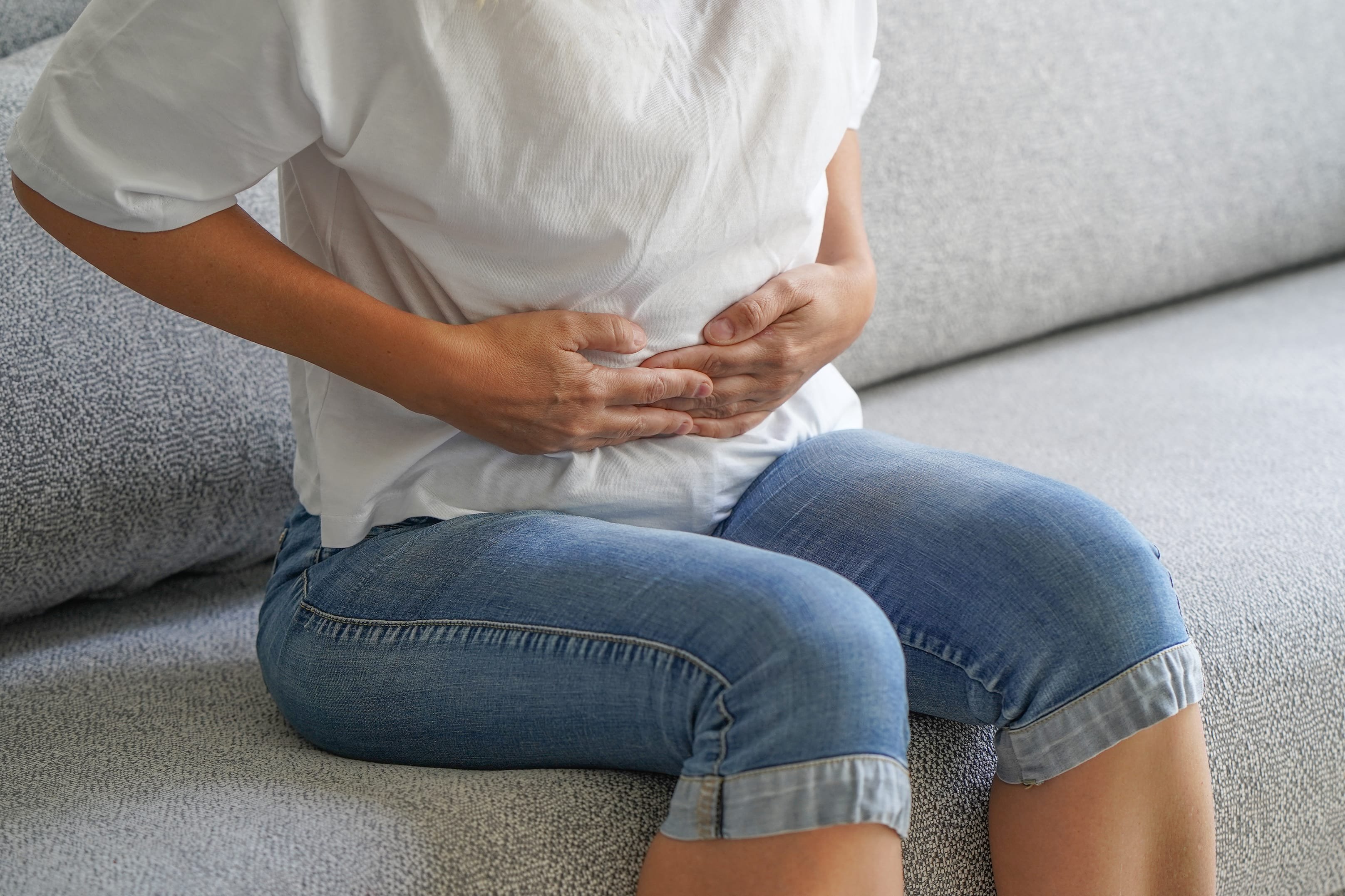 Woman sitting on sofa and holding her hands on her stomach. 