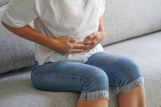  Woman sitting on sofa and holding her hands on her stomach.  